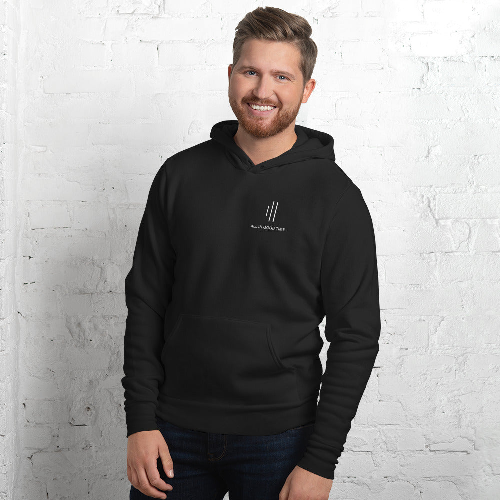 Man wearing black drummer hoodie by Cowbell & Groove, front view with minimalist chest logo, smiling in casual pose
