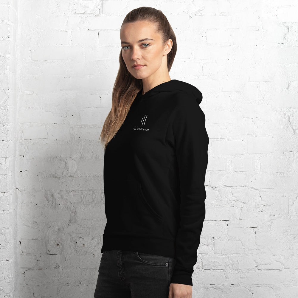 Woman wearing black drummer hoodie by Cowbell & Groove, side pose with minimalist groove bar logo and 'All in Good Time' visible on chest